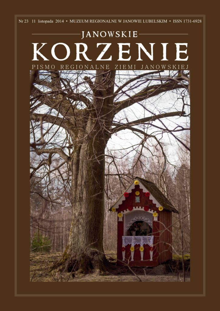 Duże drzewo bez liści obok czerwonej kapliczki ozdobionej sztucznymi kwiatami, w tle las liściasty bez liści.