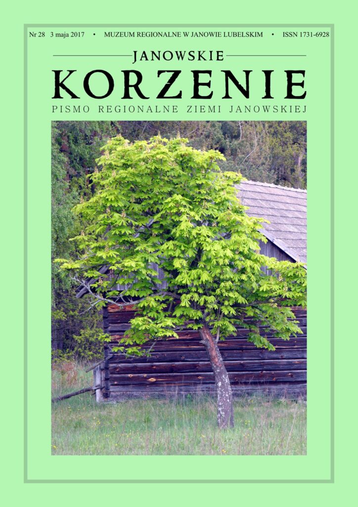 Drzewo z zielonymi liśćmi na tle starej drewnianej chaty, trawa w pierwszym planie, las w tle.
