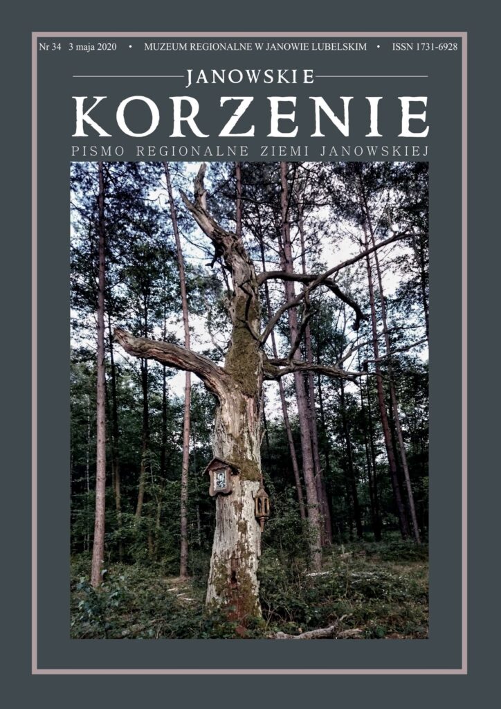 Stare, częściowo pozbawione kory drzewo z mchem, z dwoma drewnianymi elementami przytwierdzonymi do pnia, na tle wysokich sosen i zielonego podszytu.