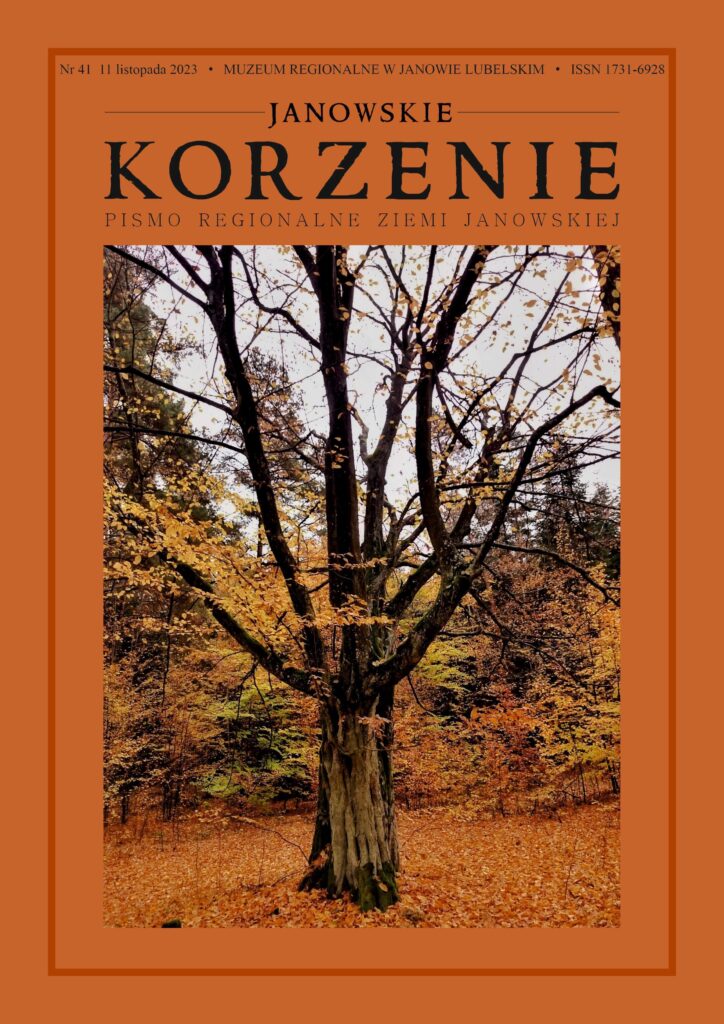 Stare drzewo z częściowo opadłymi żółto-brązowymi liśćmi na tle lasu w jesiennych kolorach.
